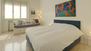 Een slaapkamer met een groot bed, een bank met kussens, een raam met jaloezieën en een schilderij aan de muur.