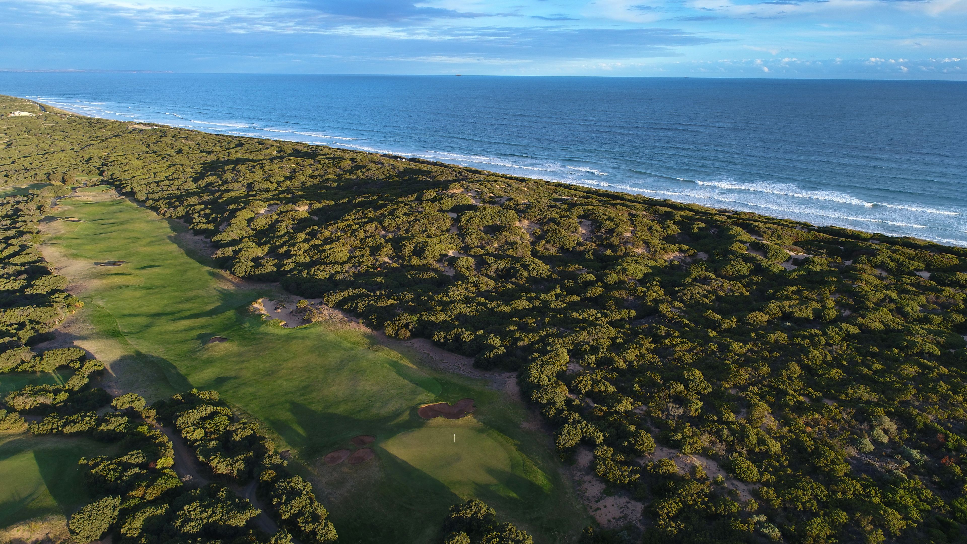 Vue aérienne d’une zone côtière caractérisée par une végétation luxuriante, un terrain de golf et l’océan.