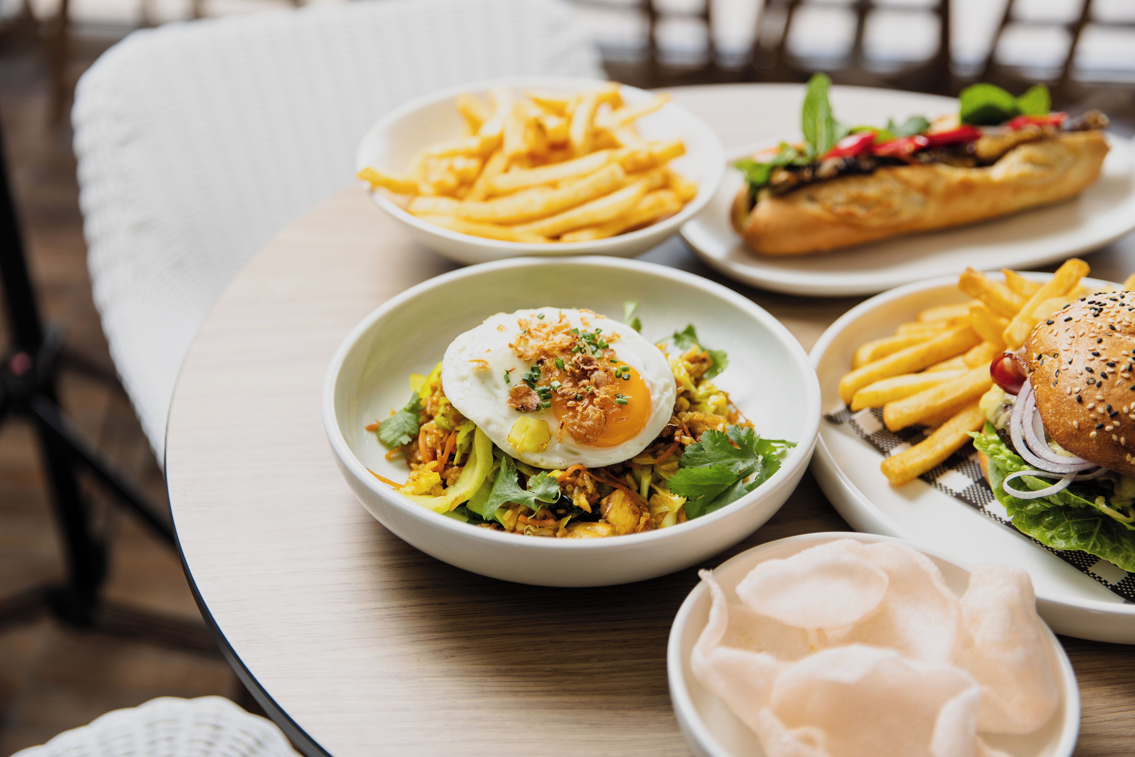 Una mesa con diferentes platos, incluyendo un bol de ensalada, una porción de papas fritas, un sándwich y una hamburguesa.