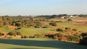 A golf course with bunkers, trees, and a building in the background.