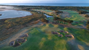 Vista aérea de un campo de golf con búnkeres de arena, árboles y una masa de agua.