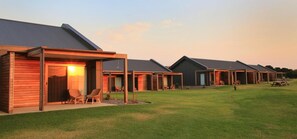 A row of modern cabins with attached porches, each featuring a door and windows, and a grassy lawn in front. - 13th Beach Golf Lodges (Connewarre)