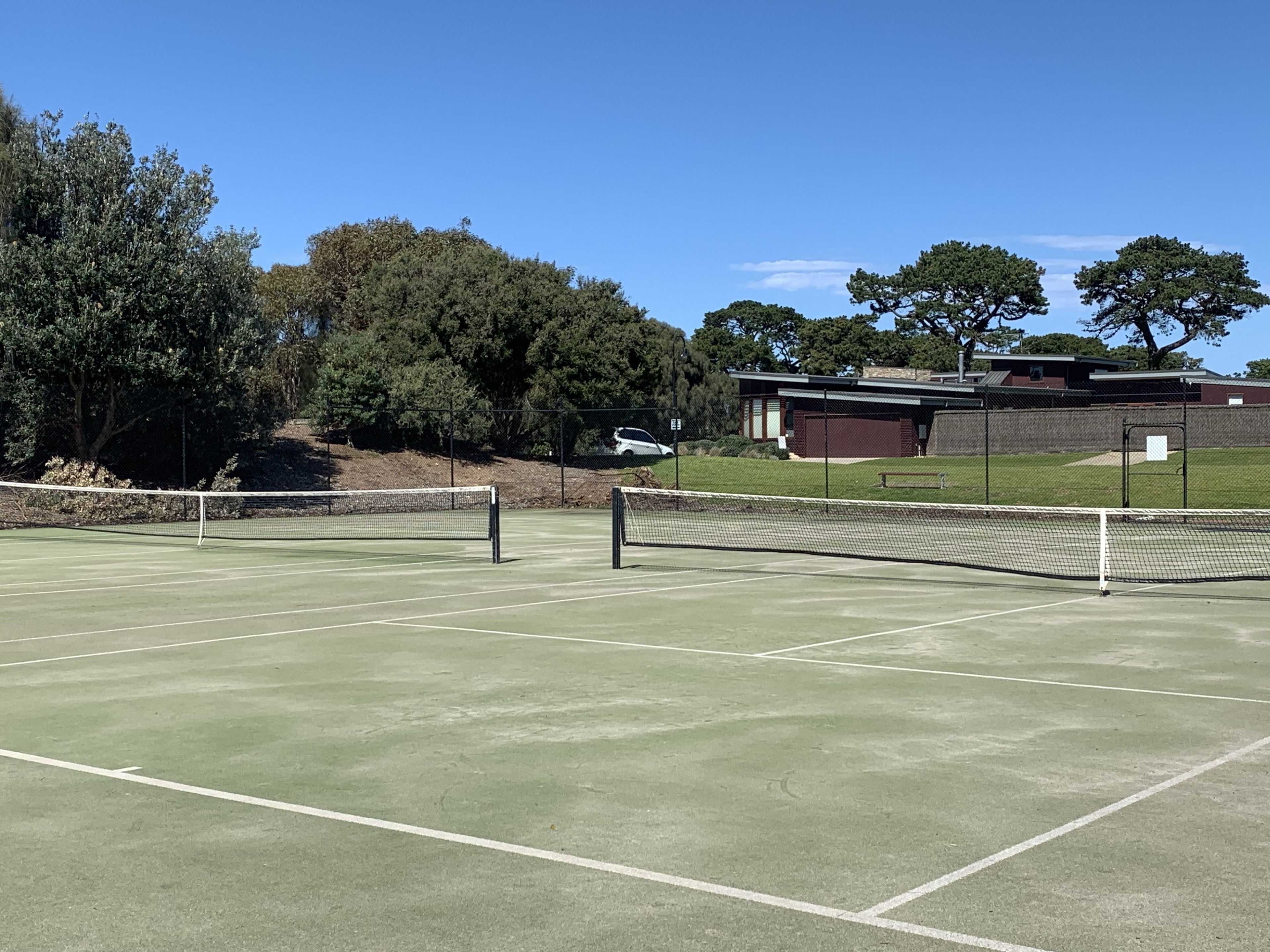 A tennis court with a net, surrounded by trees and a building in the background.