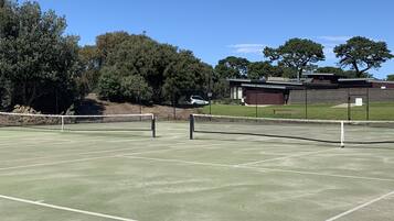 A tennis court with a net, surrounded by trees and a building in the background.