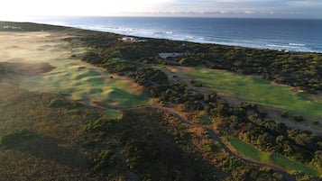 Luchtbeeld van een kustgebied met een golfbaan, een weg en een gebouw nabij het water.