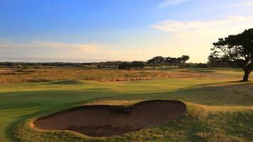 A golf course with a sand bunker, trees, and a clear sky.