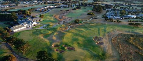 Vista aérea de un campo de golf con un club de campo, múltiples greens y zonas residenciales circundantes.