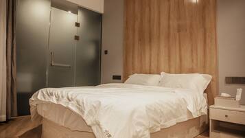 A bedroom with a bed, a wooden nightstand, a wooden wardrobe, and a wall-mounted light.