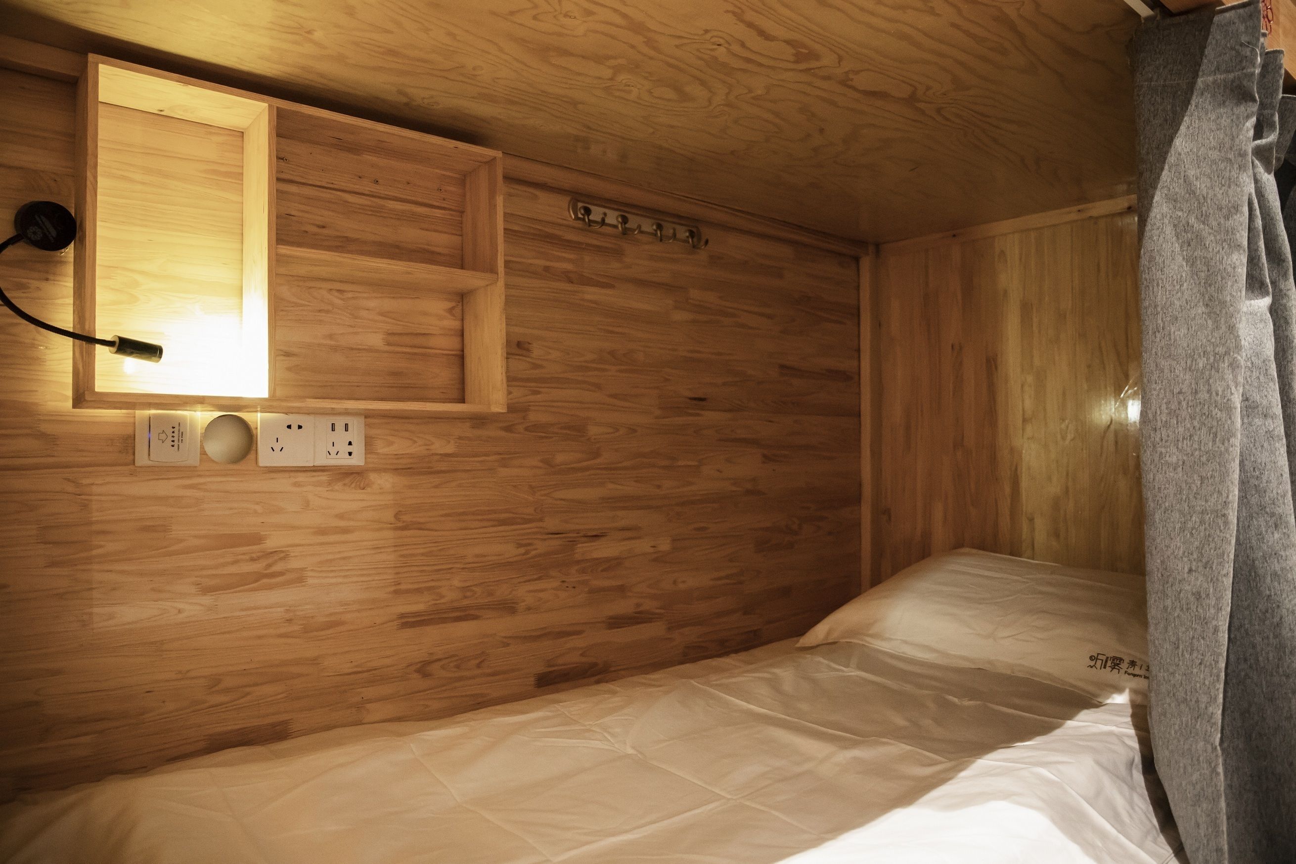 Una habitación con paneles de madera, una cama, una lámpara de pared y un enchufe.