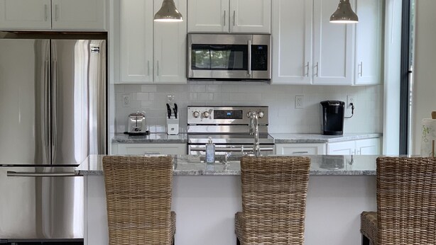 Una cocina moderna con armarios blancos, electrodomésticos de acero inoxidable y una isla central con taburetes de bar.