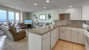 Amplia sala de estar con televisor grande, un sofá y una zona de comedor con mostrador de cocina.