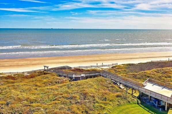 A beach view with a wooden boardwalk leading to a covered area.