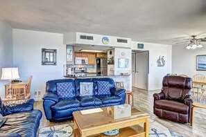 Un salon avec un canapé en cuir bleu, un fauteuil en cuir marron, une table basse en bois et, au fond, un coin cuisine.