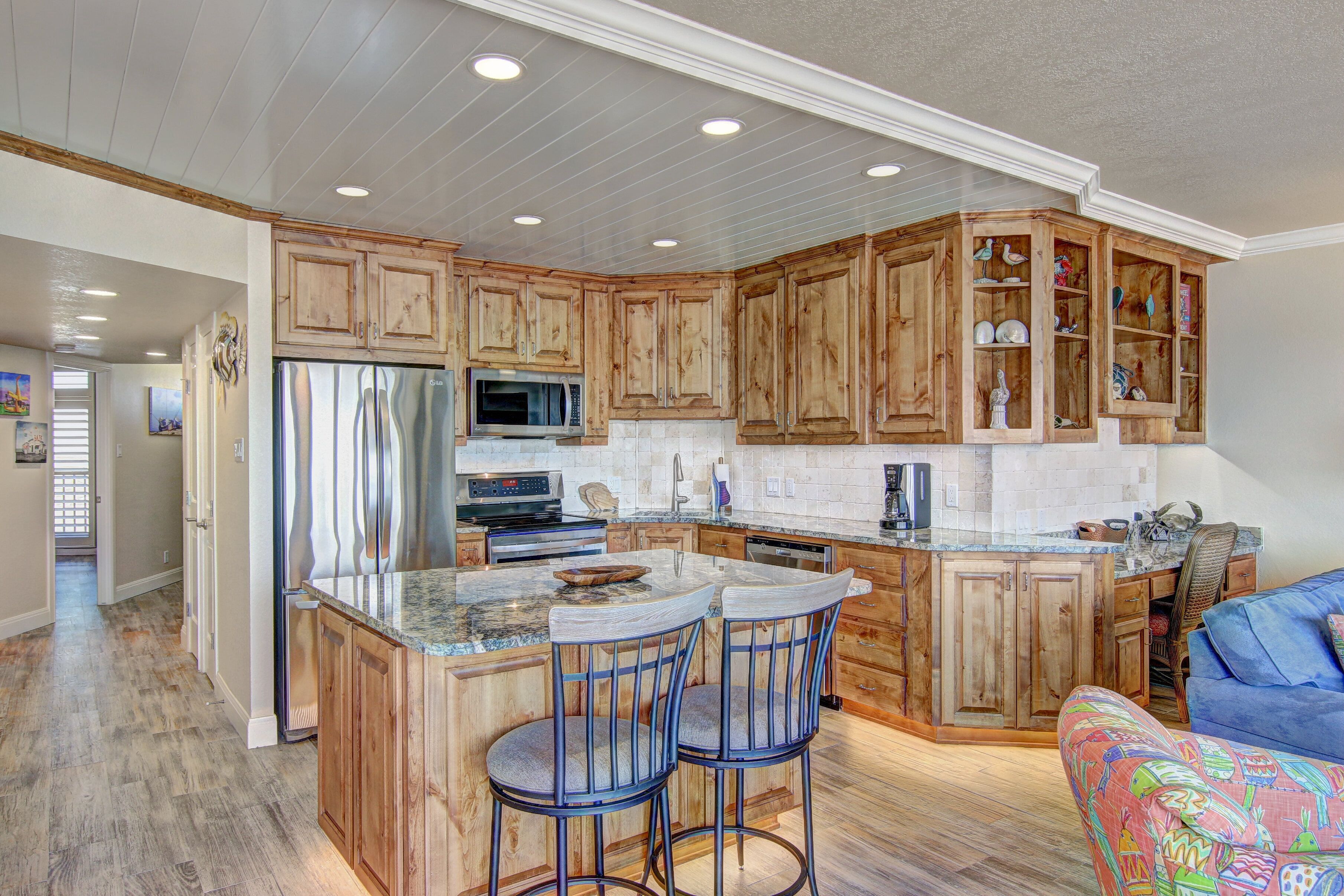 A spacious kitchen with wooden cabinets, a stainless steel refrigerator, a microwave, and a large island with bar stools.