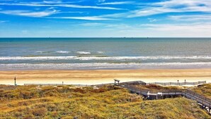 Una playa con un paseo marítimo de madera que conduce a la orilla, arena y océano.