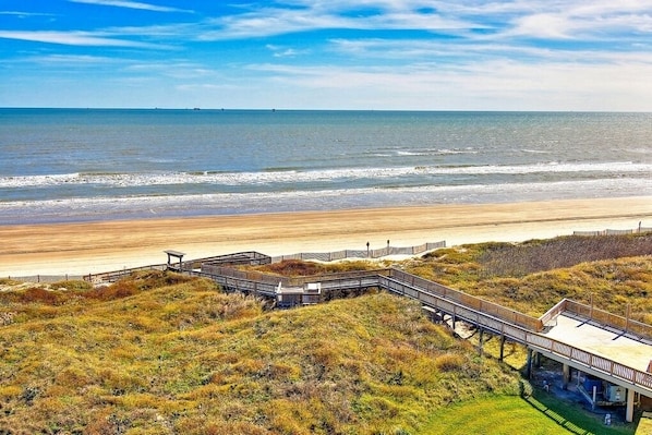 A beach view with a wooden boardwalk leading to a covered area.