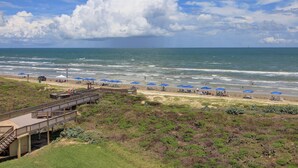 Une plage avec une promenade en bois, des parasols et une vue lointaine sur l’océan.
