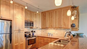 Une cuisine dotée de meubles en bois, d’appareils électroménagers en acier inoxydable, de plans de travail en granit et de luminaires suspendus.