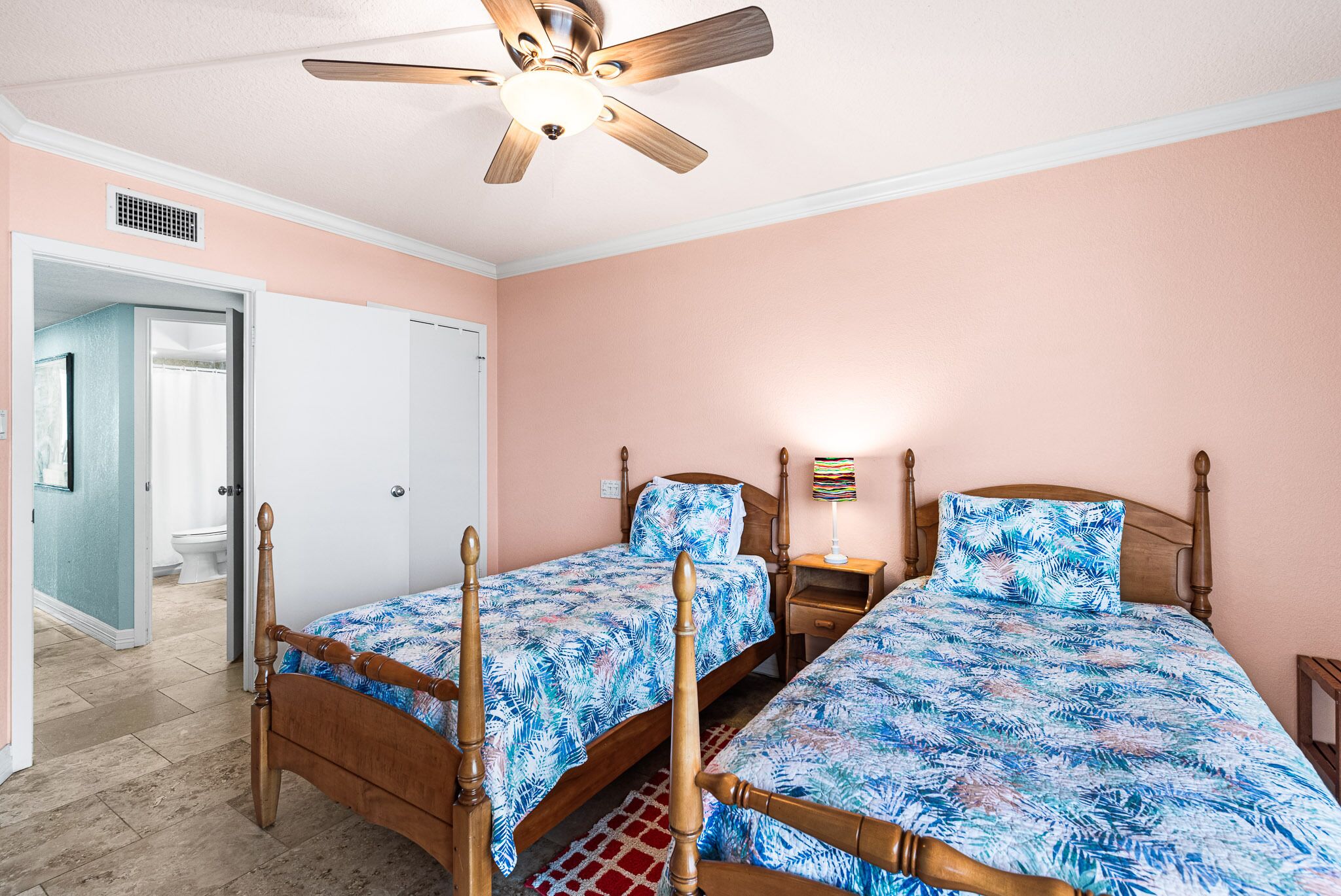 Una camera da letto con due letti in legno, una ventola a soffitto e un comodino con una lampada.