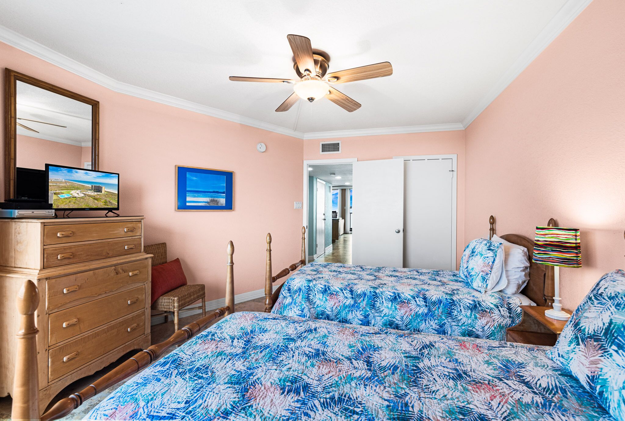 A bedroom with two beds, a ceiling fan, a dresser, a television, and a door leading to another room.