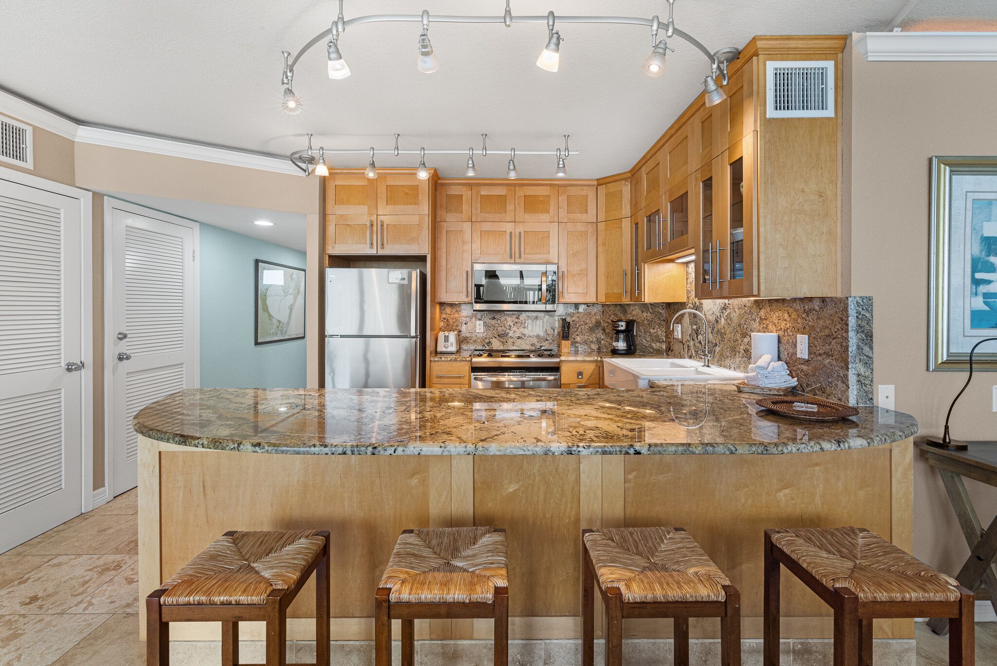 A kitchen with a large island, wooden cabinets, stainless steel appliances, and a marble countertop.