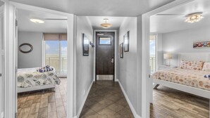 A hallway with two bedrooms, each with a bed, a window with blinds, and a door at the end.
