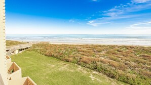 A view from a balcony overlooking a beach with a wooden walkway leading to the shore.