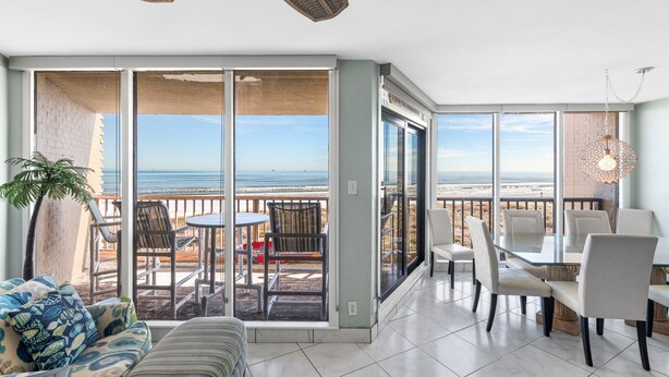 A spacious balcony with a view of the beach, furnished with a table and chairs, and a potted plant.