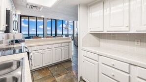 A modern kitchen with white cabinetry, a large window with a view, and a stone tile floor. - Sea Gull #1110: Beachfront 3 Bedroom 2.5 Bathroom With Spectacular Views and 24 Hour Management (Port Aransas)