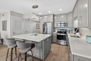 A modern kitchen with a central island, stainless steel appliances, and grey cabinetry.