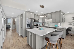 A modern kitchen with a central island, stainless steel appliances, and a herringbone-patterned backsplash. - Sea Gull #906LK: Beachfront 1 Bedroom 1 Bathroom With Spectacular Views and 24 Hour Management (Port Aransas)