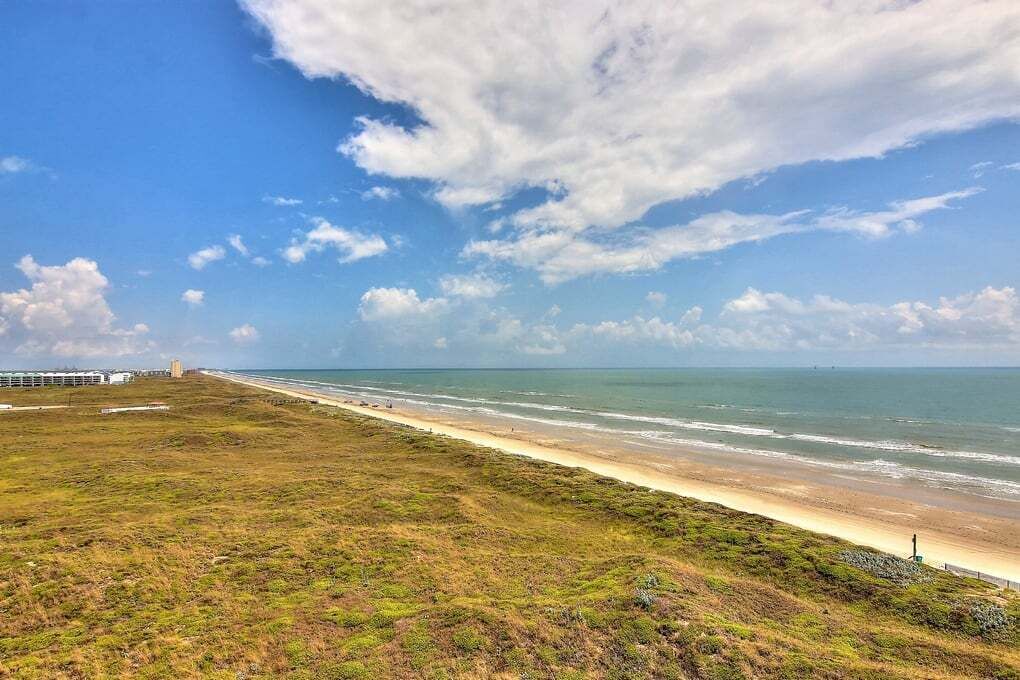A coastal landscape with a beach, grassy terrain, and a distant structure.