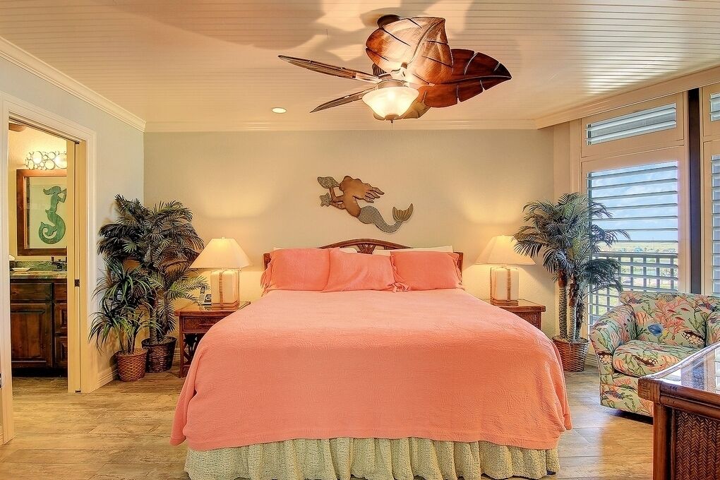 Ein Schlafzimmer mit einem großen Bett, zwei Nachttischen, einem Deckenventilator und einer an der Wand befestigten Leuchte.