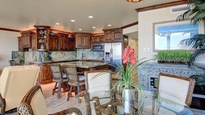A spacious kitchen with wooden cabinets, a marble countertop, and a dining area with a glass table and chairs. - Sea Gull #802: Beachfront 2 Bedroom 2 Bathroom With Spectacular Views and 24 Hour Management (Port Aransas)