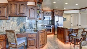 A kitchen with wooden cabinets, a marble countertop, and a central island with bar stools. - Sea Gull #802: Beachfront 2 Bedroom 2 Bathroom With Spectacular Views and 24 Hour Management (Port Aransas)