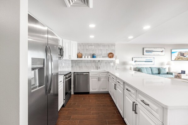 A modern kitchen with white cabinetry, stainless steel appliances, and a wooden floor. - Sea Gull #609L: Beachfront 1 Bedroom 1 Bathroom With Spectacular Views and 24 Hour Management (Port Aransas)