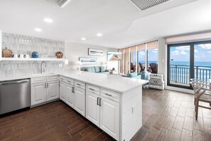 A modern kitchen with white cabinetry, a large island, and a view of the ocean through the sliding glass doors. - Sea Gull #609L: Beachfront 1 Bedroom 1 Bathroom With Spectacular Views and 24 Hour Management (Port Aransas)