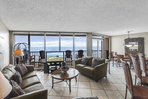 Un vaste salon doté d’une grande fenêtre donnant sur la mer, aménagé avec un canapé, une table basse et un coin repas.