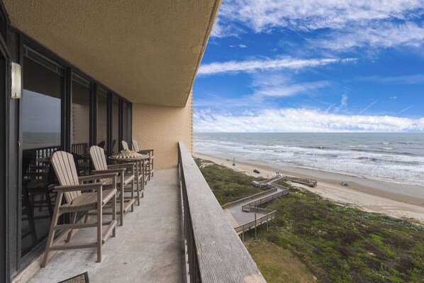 Un balcon avec des chaises en bois et une vue sur la plage et l’océan.