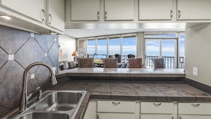 Una cocina con una isla grande, pileta de acero inoxidable y muebles altos blancos.