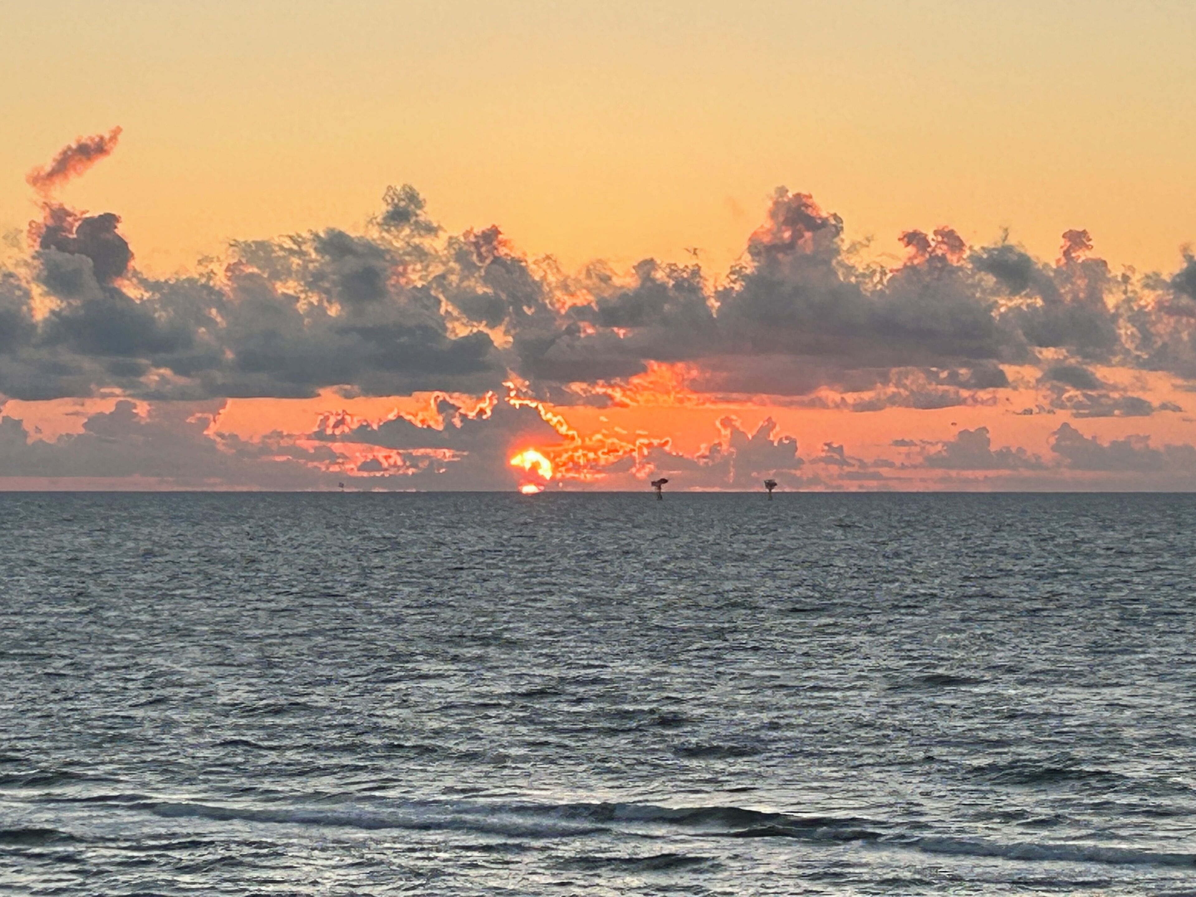 A sunset over the ocean with a clear sky and calm water.