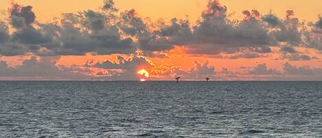 A sunset over the ocean with a clear sky and calm water.