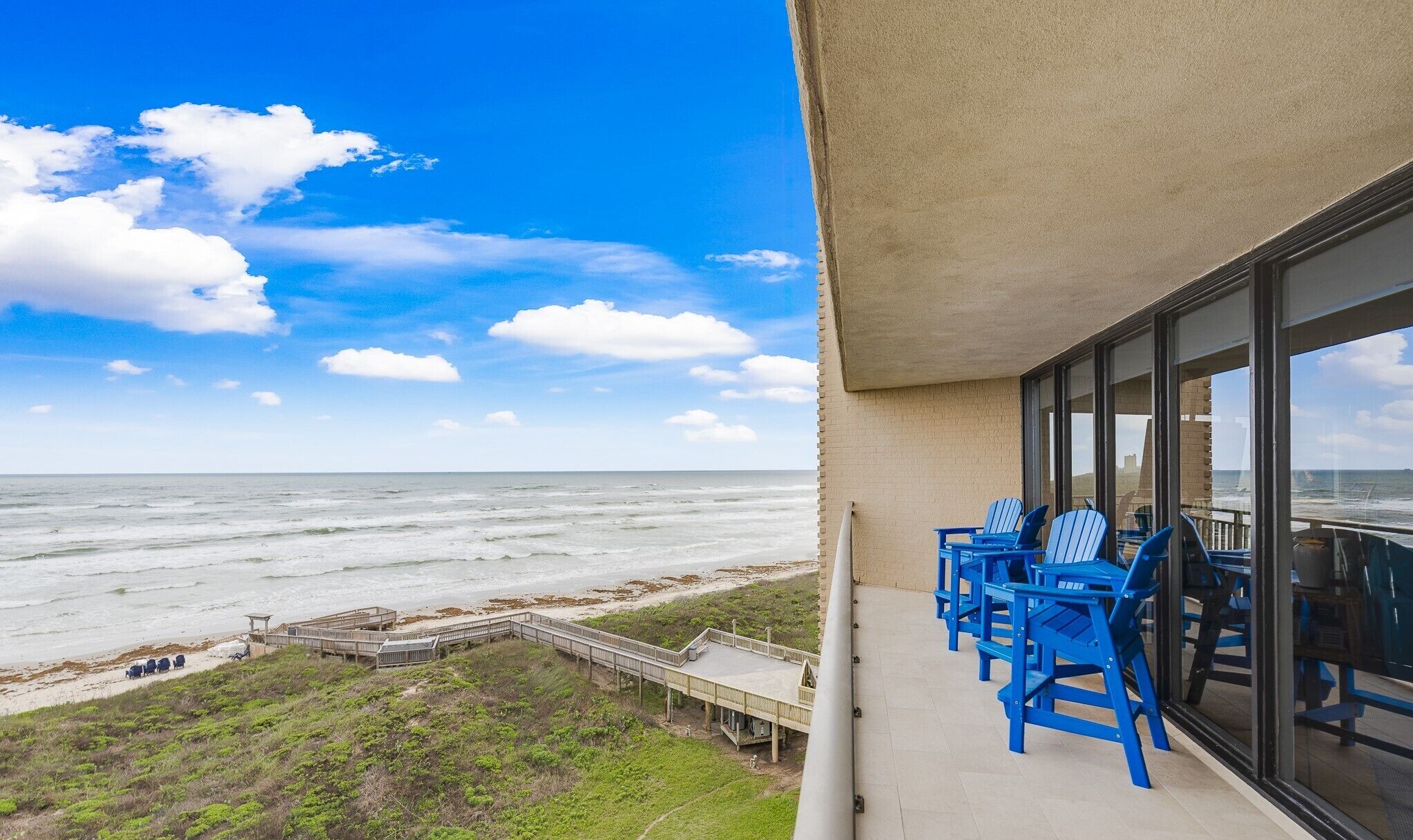 Un balcon avec des chaises bleues donnant sur une plage et l’océan.