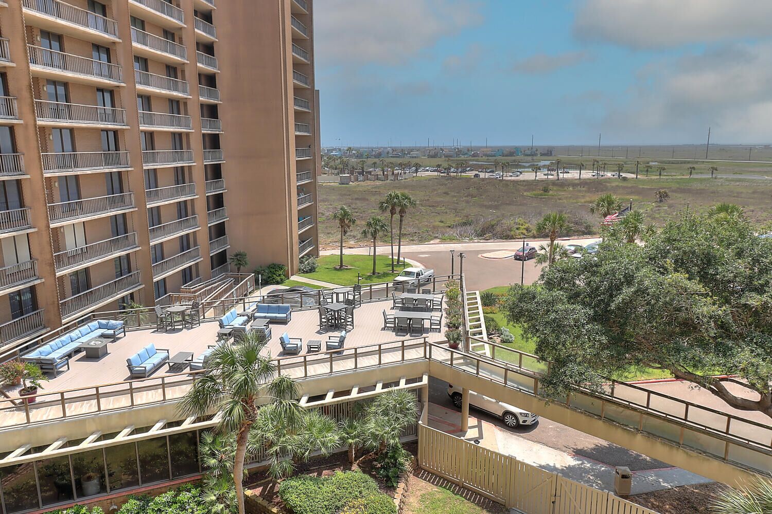 Un hotel de gran altura con varios balcones, zonas de estar al aire libre y vistas a un estacionamiento y un paisaje distante.