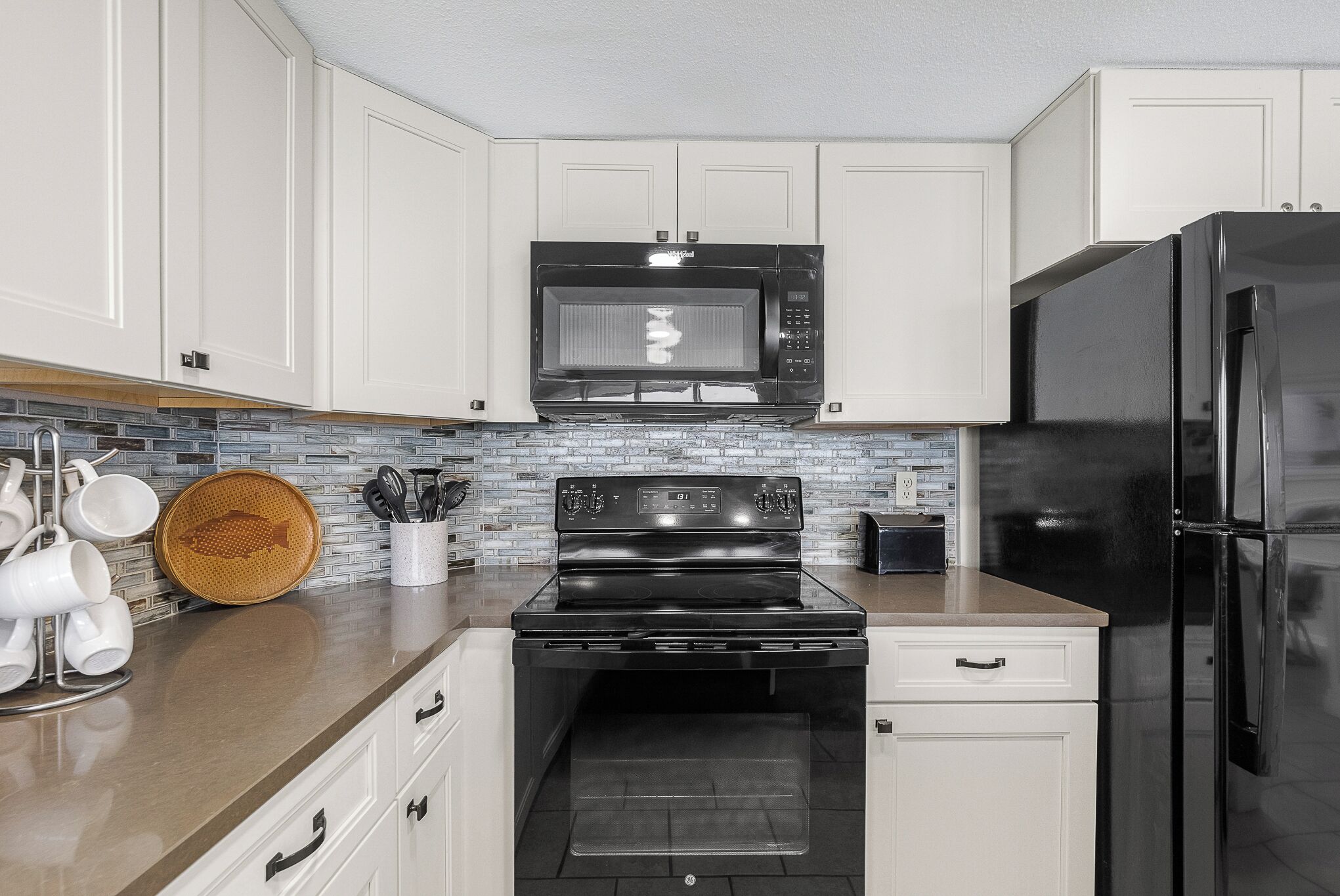 A kitchen with white cabinets, a black microwave, a black stove, a black refrigerator, and a backsplash with a mosaic tile pattern.