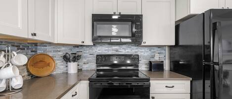 A kitchen with white cabinets, a black microwave, a black stove, a black refrigerator, and a backsplash with a mosaic tile pattern.