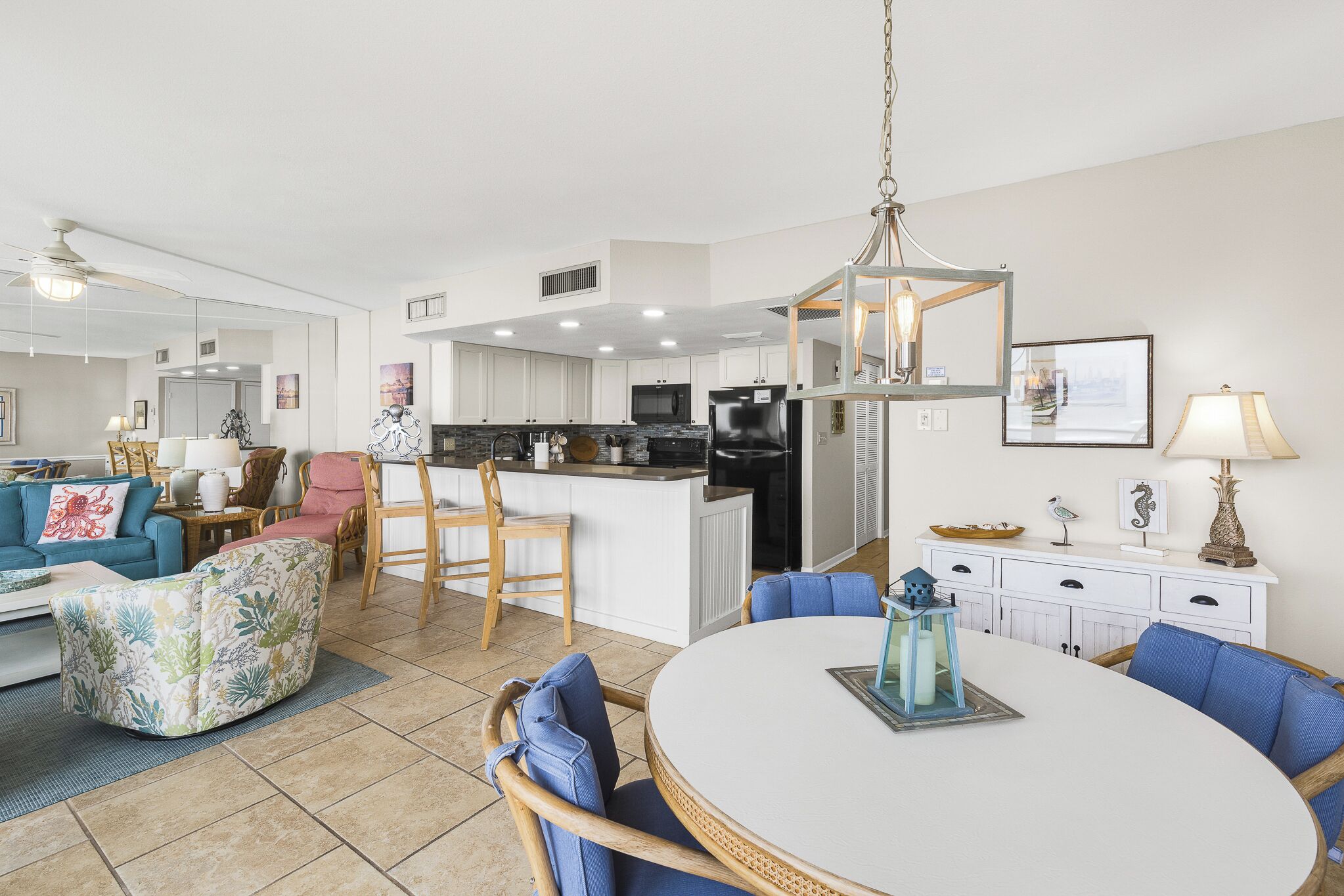 A modern kitchen with white cabinets, a central island, and a dining area with a round table and blue chairs.
