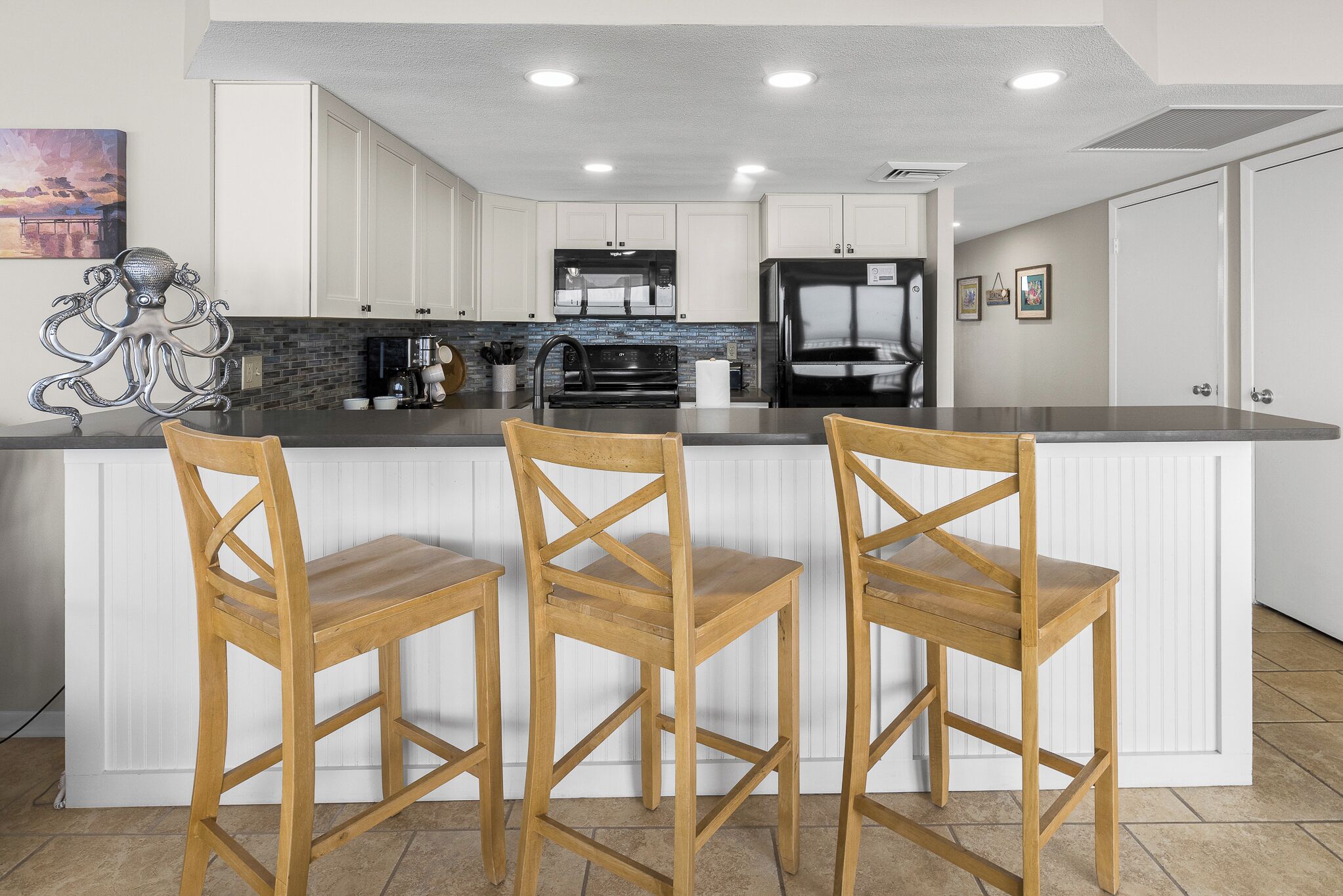 Une cuisine moderne avec des meubles blancs, un réfrigérateur noir et un îlot central doté de trois tabourets de bar en bois.