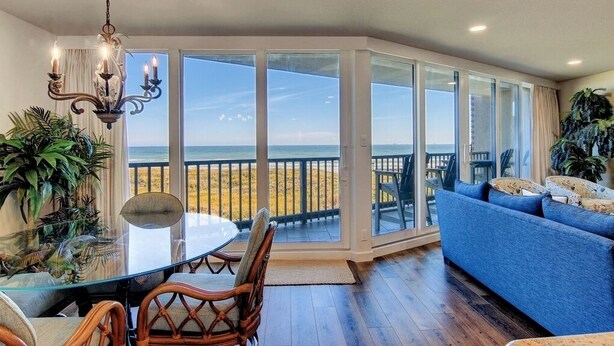 A room with a glass table, chairs, a blue sofa, and a view of the beach. - Sea Gull #202: Beachfront 2 Bedroom 2 Bathroom With Spectacular Views and 24 Hour Management (Port Aransas)
