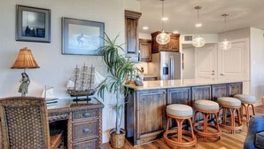 A kitchen with wooden cabinets, a central island with stools, pendant lights, and framed pictures on the wall. - Sea Gull #202: Beachfront 2 Bedroom 2 Bathroom With Spectacular Views and 24 Hour Management (Port Aransas)